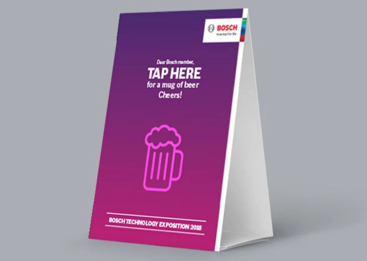 A table tent card: “Tap here for a mug of beer”, for the Bosch Technology Exposition