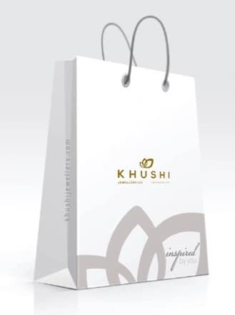 White shopping bag with grey rope handles, the Khushi logo on the front and a large petal pattern with the script word ‘inspired’ across the lower half