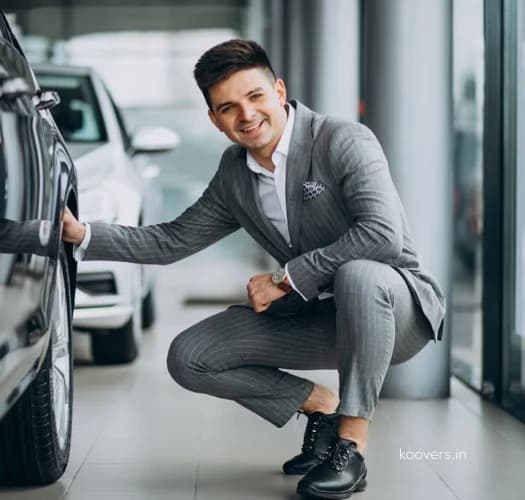 A fleet manager in a suit crouching beside a car