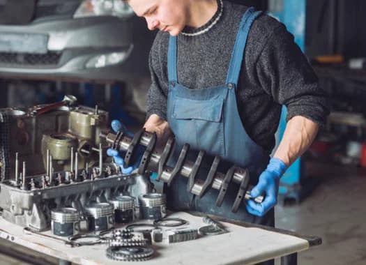 A mechanic in overalls working on an engine crankshaft